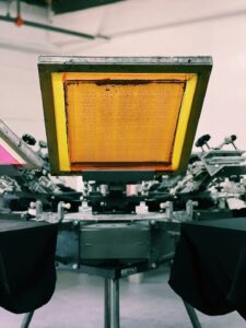 Hands compare a screen-printed shirt and a heat-transfer shirt on a worktable.