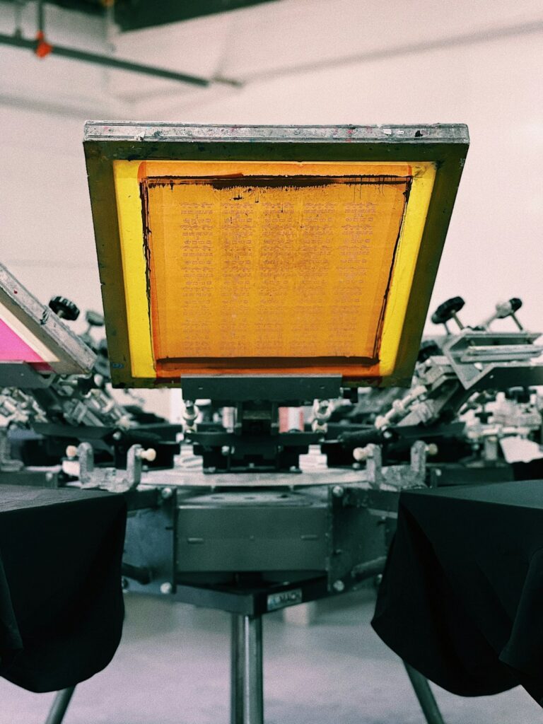 Hands compare a screen-printed shirt and a heat-transfer shirt on a worktable.
