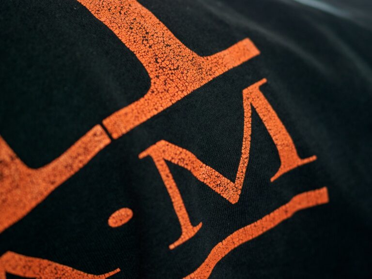 Screen printer applying white ink through a mesh screen onto a black cotton shirt.